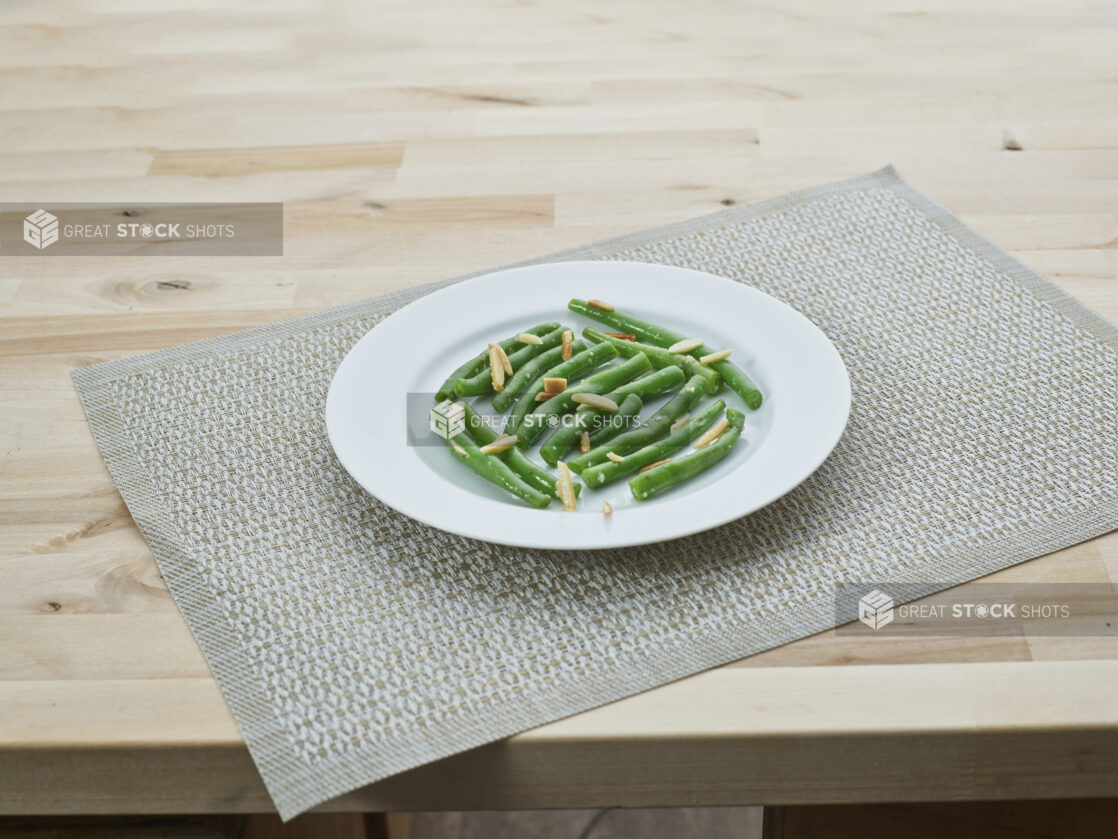 Green beans with slivered almonds on a white plate, woven placemat