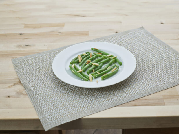 Green beans with slivered almonds on a white plate, woven placemat
