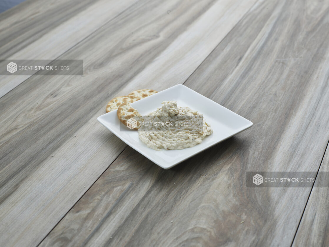 Smoked white fish salad on a square white ceramic plate with water crackers, close-up