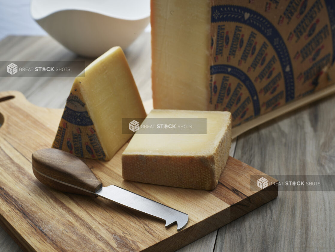 Quarter wheel of Gruyere cheese with block and wedge on a wooden cutting board, close-up