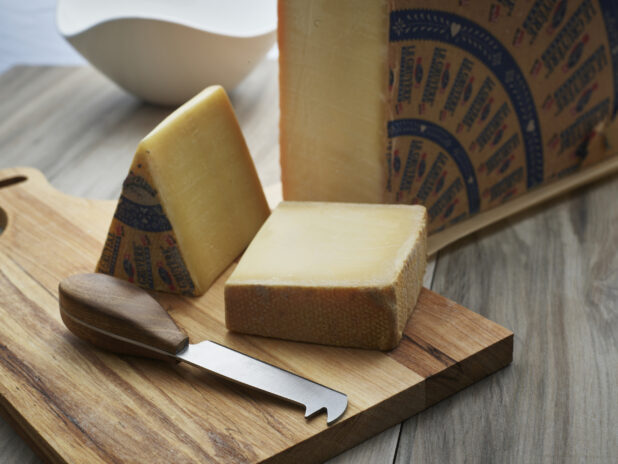 Quarter wheel of Gruyere cheese with block and wedge on a wooden cutting board, close-up