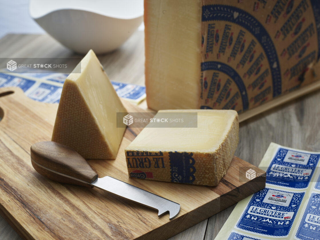 Quarter wheel of Gruyere cheese with block and wedge of cheese surrounded with sheets of brand labels, close-up