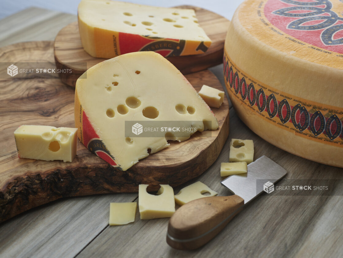 Wedges and small slices of Jarlsberg cheese on wood board with wheel of Jarlsberg