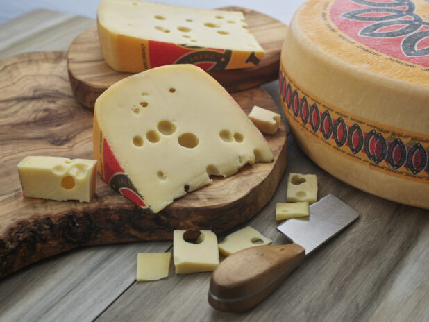 Wedges and small slices of Jarlsberg cheese on wood board with wheel of Jarlsberg