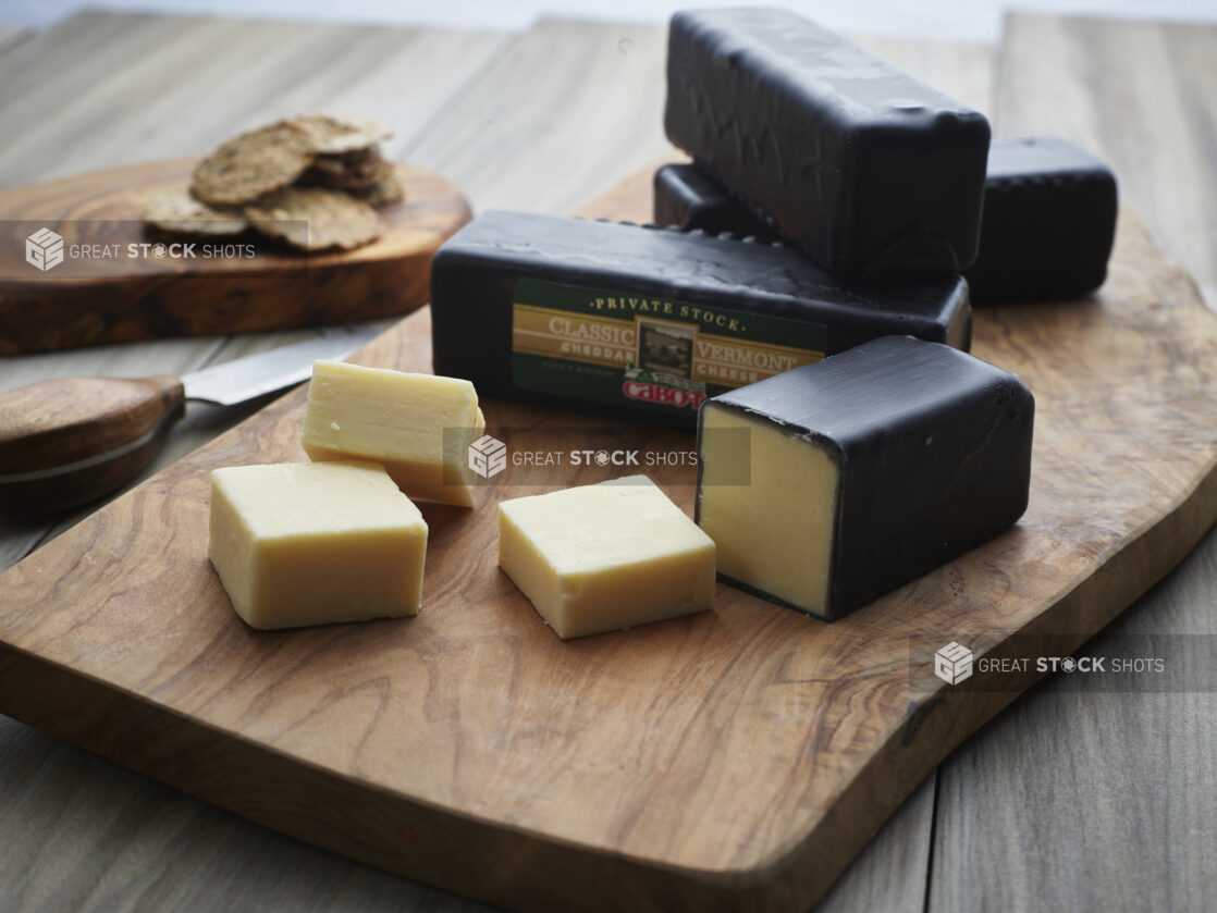 Small bricks of white cheddar cheese coated in black wax, some cut into thick slices, wax removed, close-up