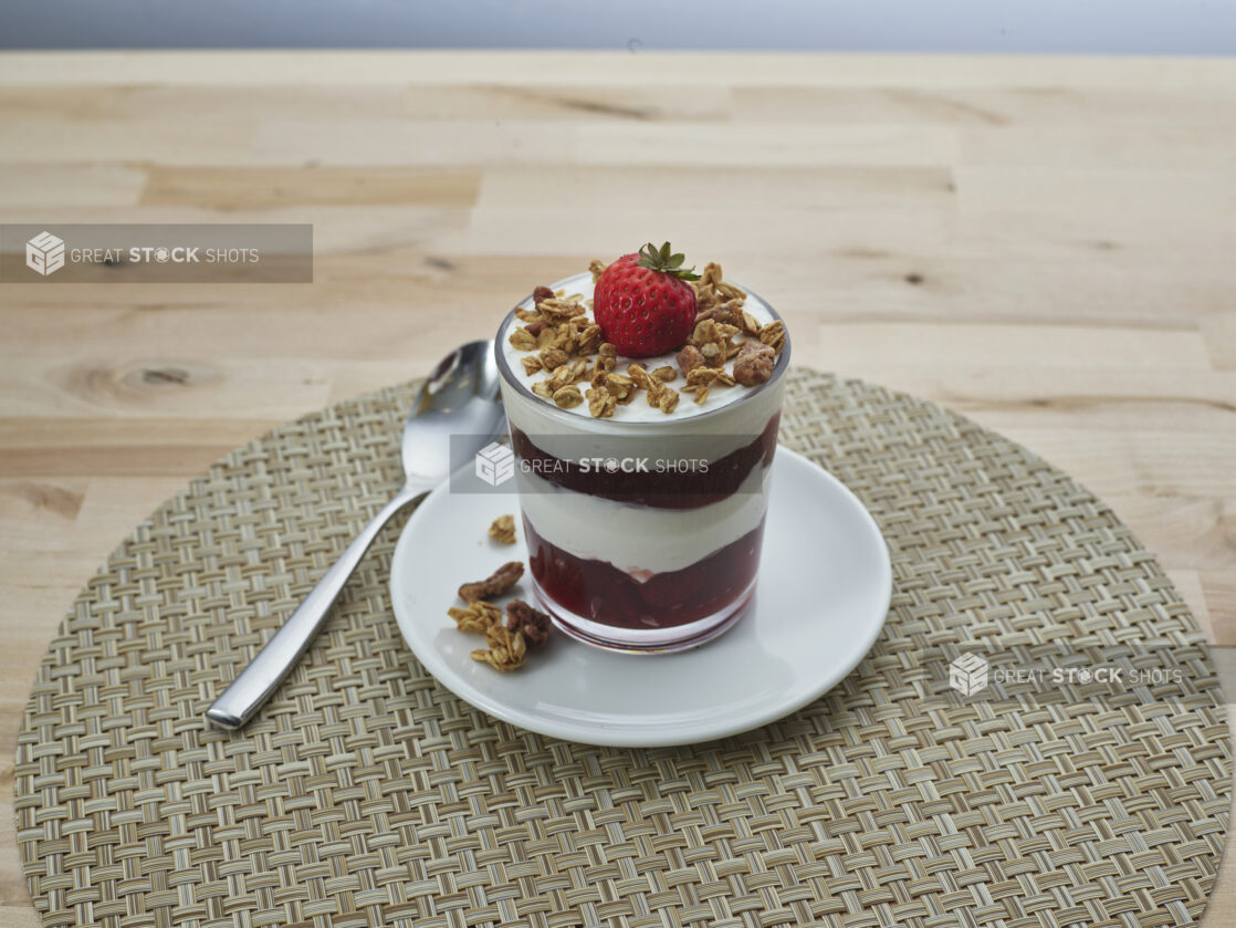 Layered strawberry compote and yogurt parfait topped with granola in a short glass, close-up