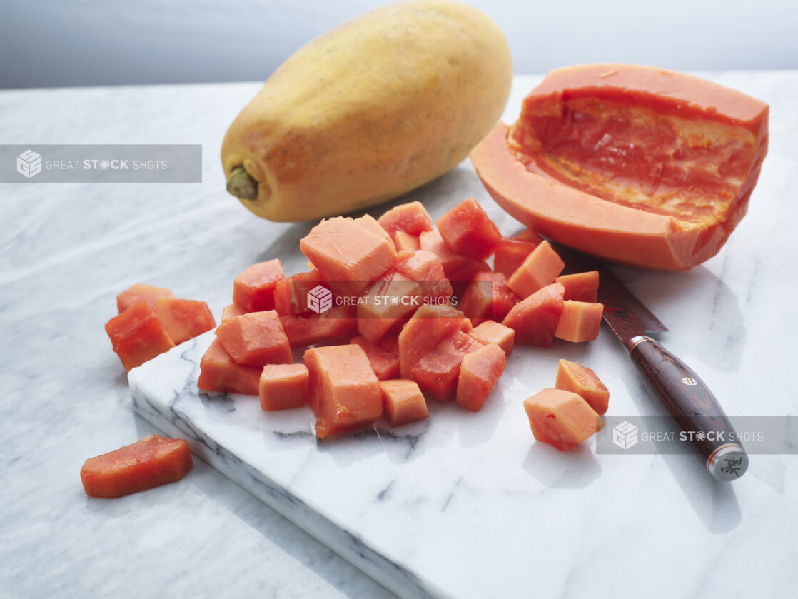 Chopped papaya with whole fruit in background on a white marble board