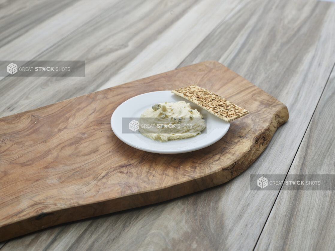 Cheddar and blue cheese spread on a small white plate with a flatbread cracker, close-up