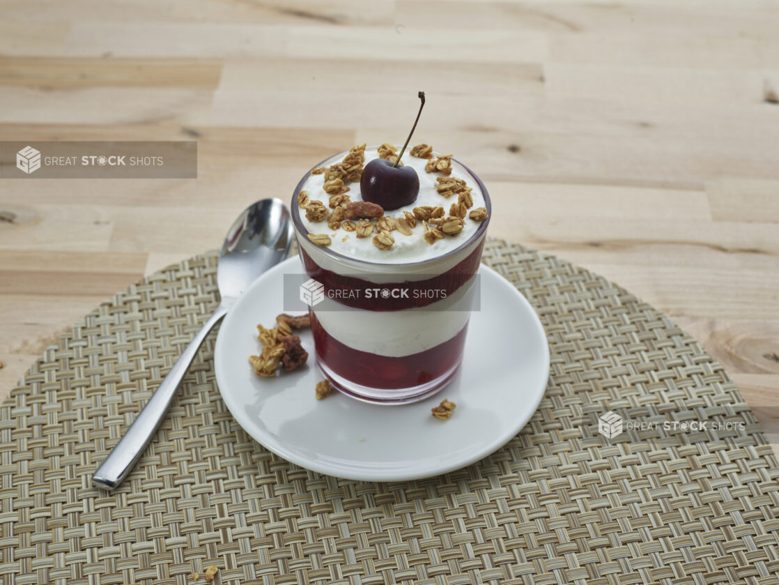 Layered cherry compote and yogurt parfait topped with granola in a short glass, close-up