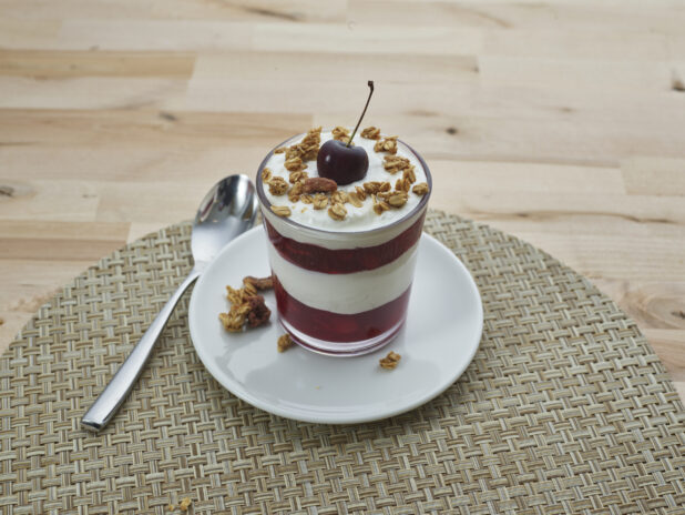 Layered cherry compote and yogurt parfait topped with granola in a short glass, close-up