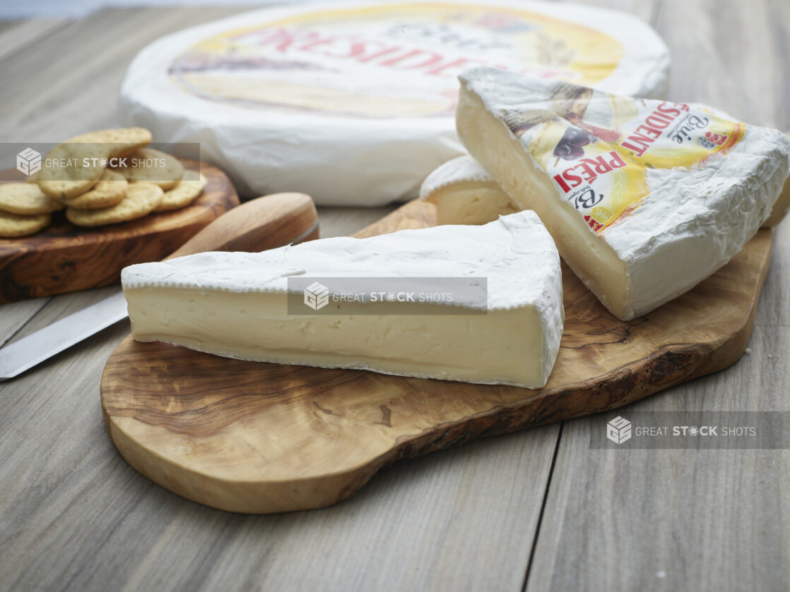 Wedges of brie cheese on natural wood boards, wheel of brie and crackers in background