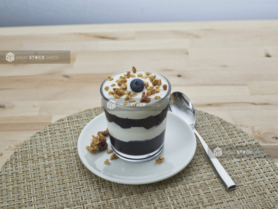 Layered blueberry compote and yogurt parfait topped with granola in a short glass, close-up