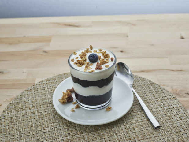 Layered blueberry compote and yogurt parfait topped with granola in a short glass, close-up