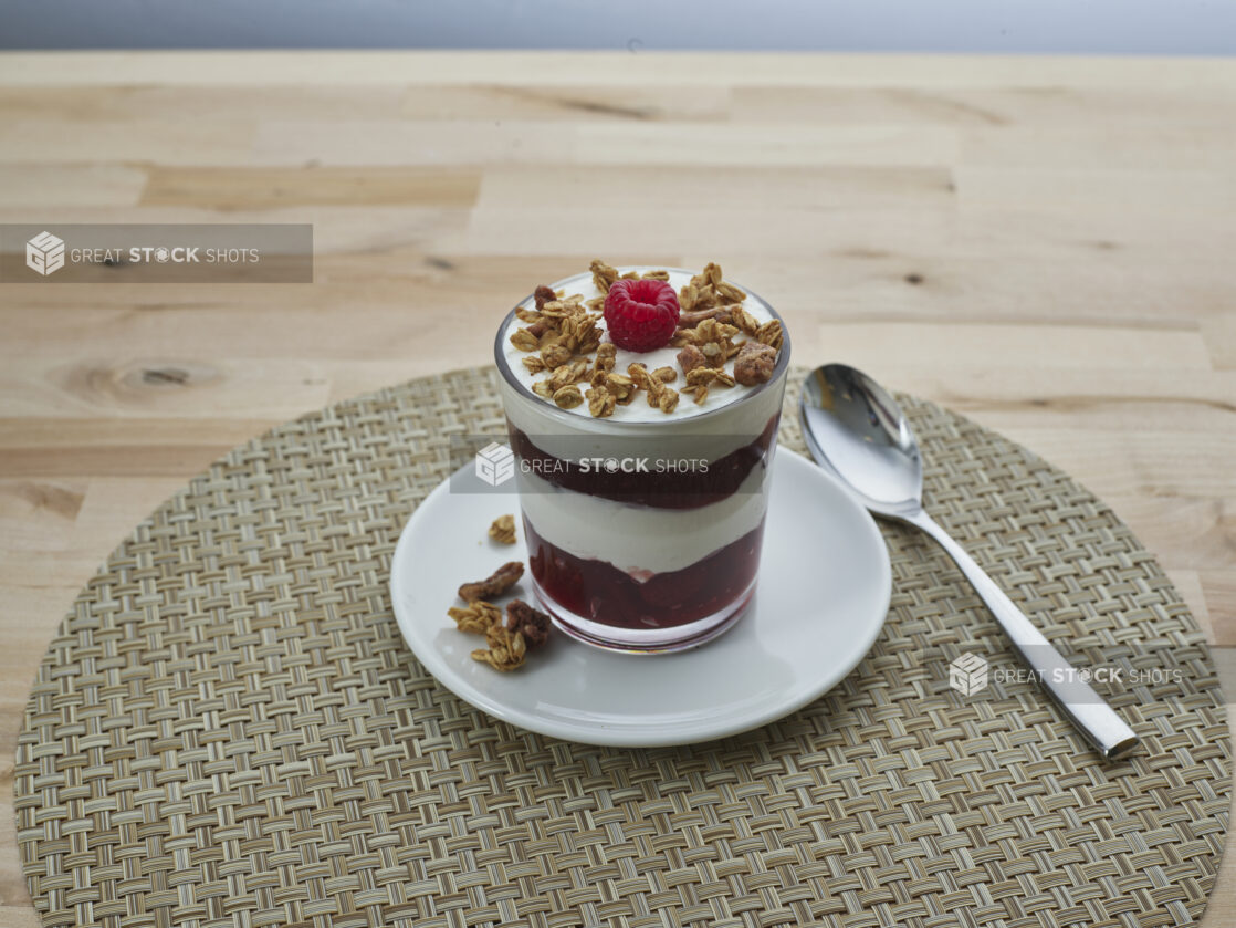 Layered raspberry compote and yogurt parfait topped with granola in a short glass, close-up