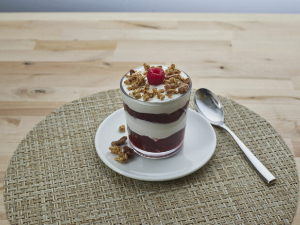 Layered raspberry compote and yogurt parfait topped with granola in a short glass, close-up