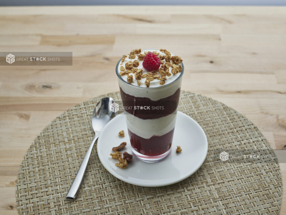 Layered raspberry compote and yogurt parfait topped with granola in a tall glass, close-up