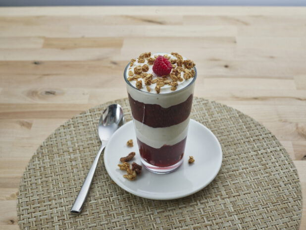 Layered raspberry compote and yogurt parfait topped with granola in a tall glass, close-up