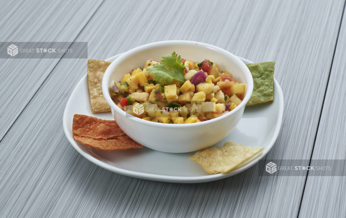 Pineapple and mango salsa in a small white bowl, plated with corn chips, close-up