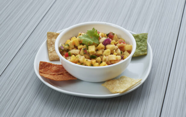 Pineapple and mango salsa in a small white bowl, plated with corn chips, close-up