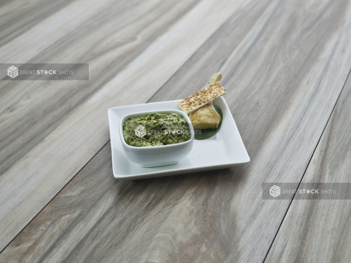 Spinach and artichoke cheese spread in white ramekin, plated with cracker and ingredients