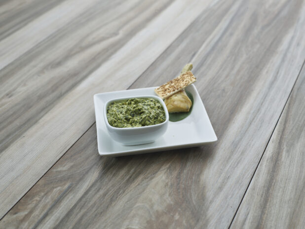 Spinach and artichoke cheese spread in white ramekin, plated with cracker and ingredients