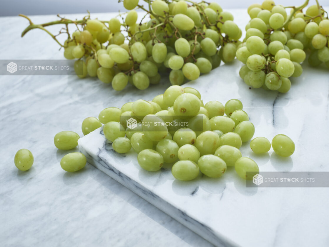 Loose green grapes on a white marble board, bunches of grapes in background, close-up