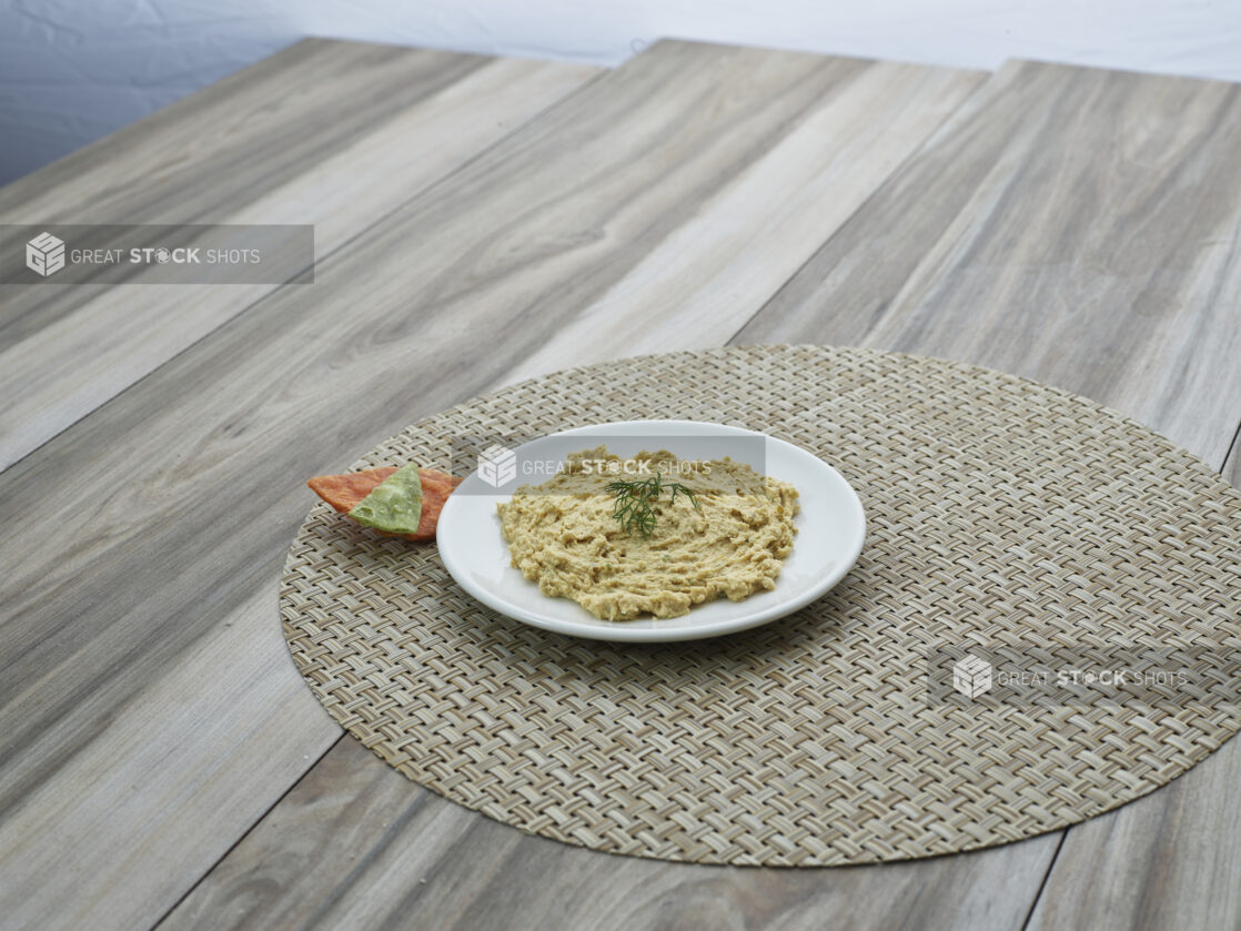 Small white plate of dill hummus on a round woven placemat