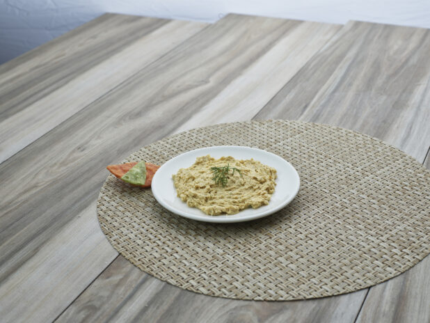 Small white plate of dill hummus on a round woven placemat