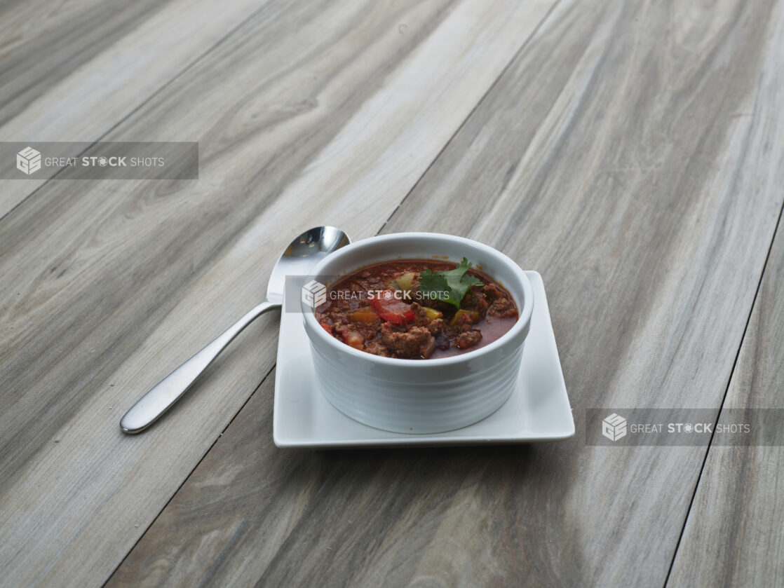 Small white bowl of Chili con Carne on a square white plate, close-up