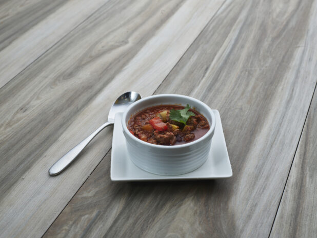 Small white bowl of Chili con Carne on a square white plate, close-up
