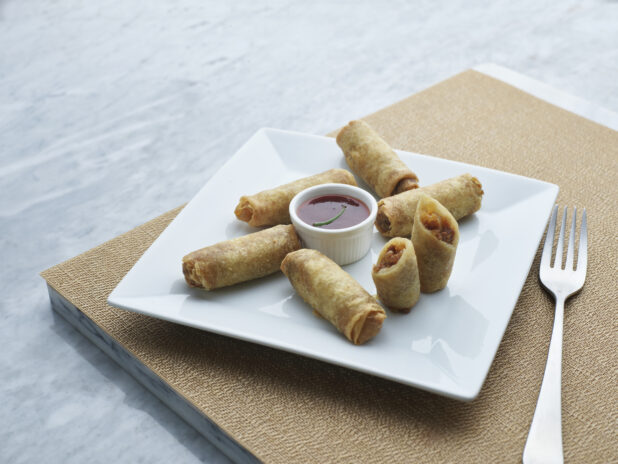 Fried spring rolls on a square white plate with a ramekin of chili dipping sauce, close-up