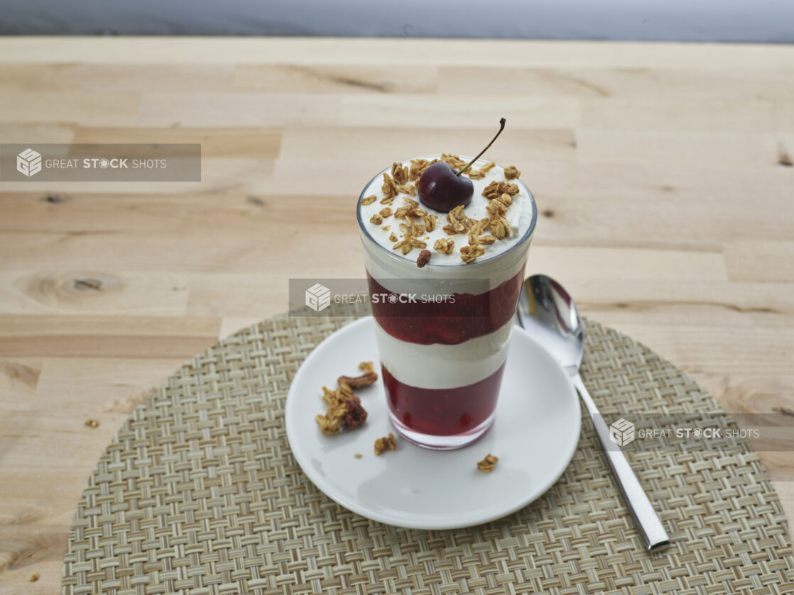 Layered cherry compote and yogurt parfait topped with granola in a tall glass, close-up