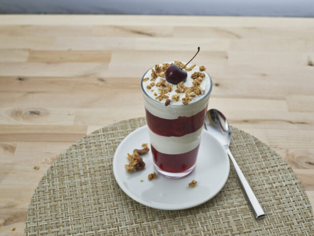 Layered cherry compote and yogurt parfait topped with granola in a tall glass, close-up