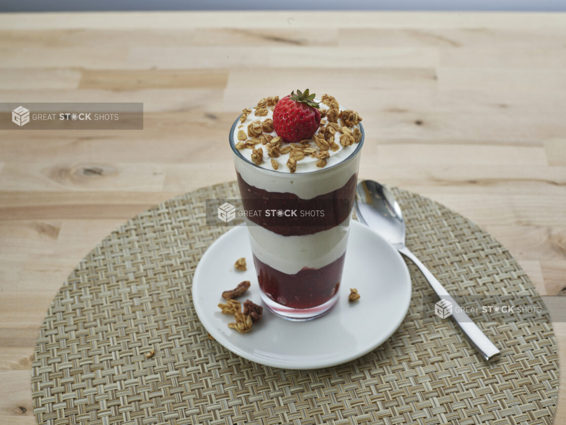 Layered strawberry compote and yogurt parfait topped with granola in a glass, close-up