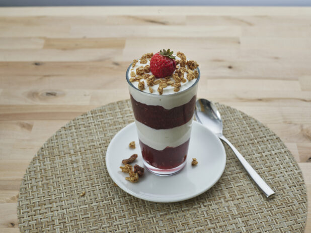 Layered strawberry compote and yogurt parfait topped with granola in a glass, close-up