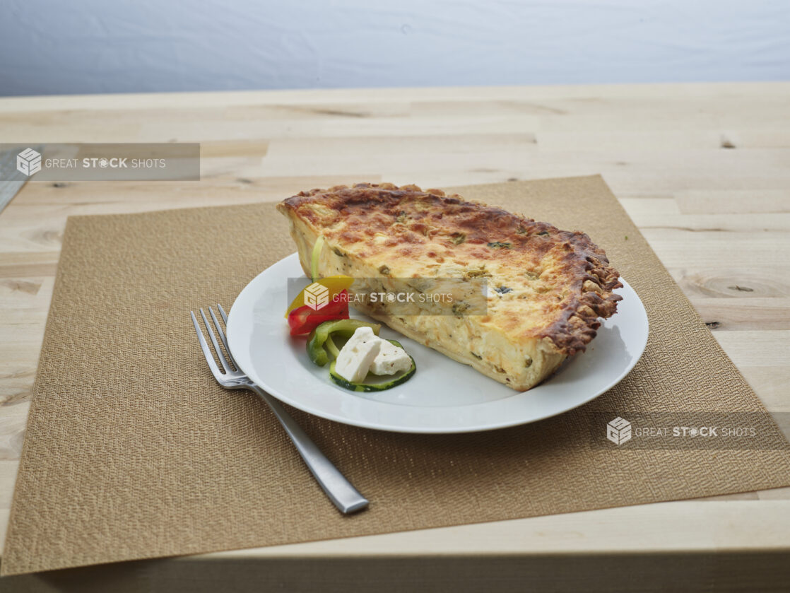 Half feta cheese and vegetable quiche with ingredients on a white plate