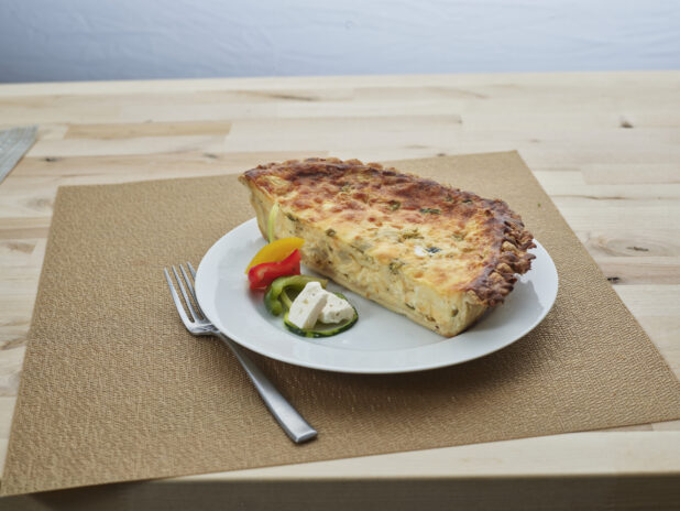 Half feta cheese and vegetable quiche with ingredients on a white plate