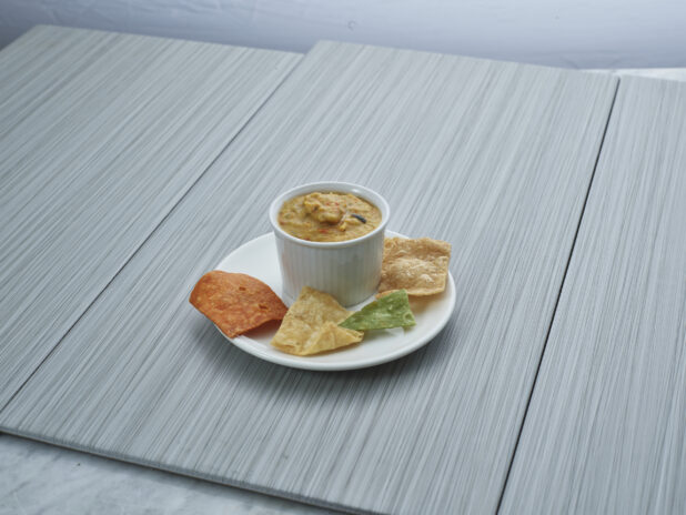 Grilled vegetable dip in a white ceramic ramekin, plated with a few corn chips