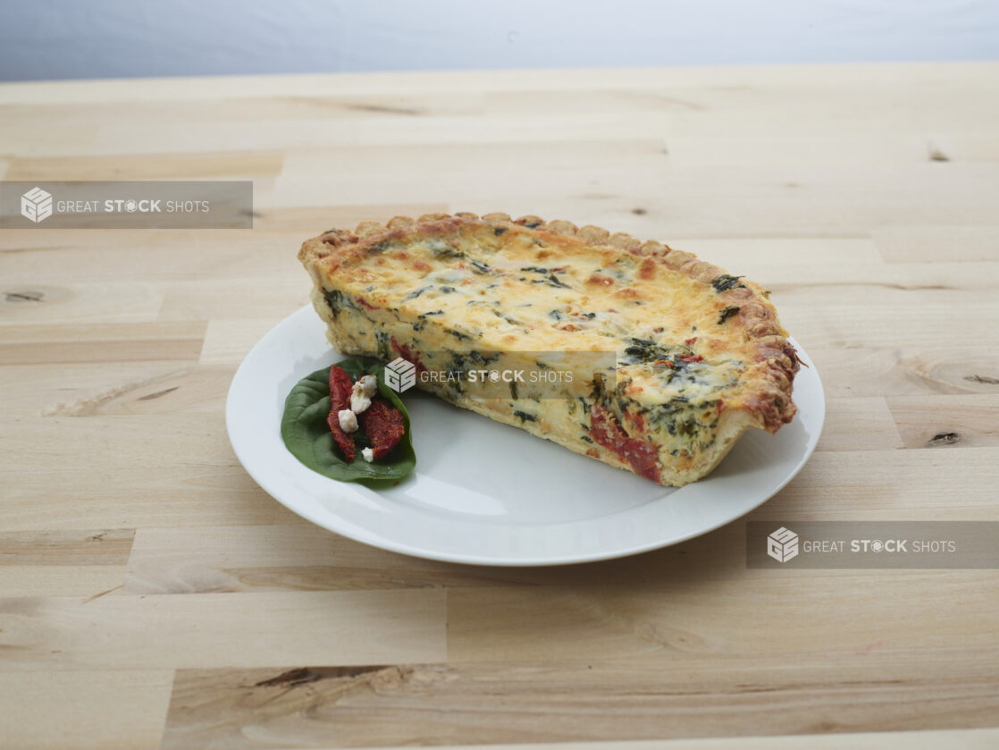 Half Mediterranean-style quiche on a white plate with garnishes, wood background