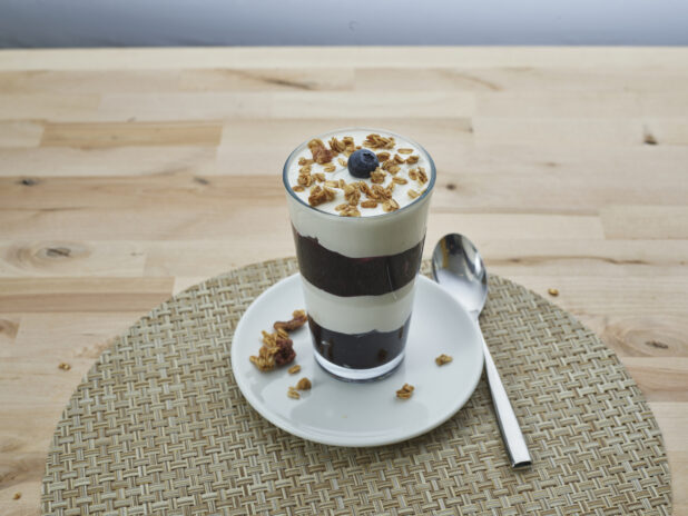 Layered blueberry compote and yogurt parfait topped with granola in a tall glass, close-up