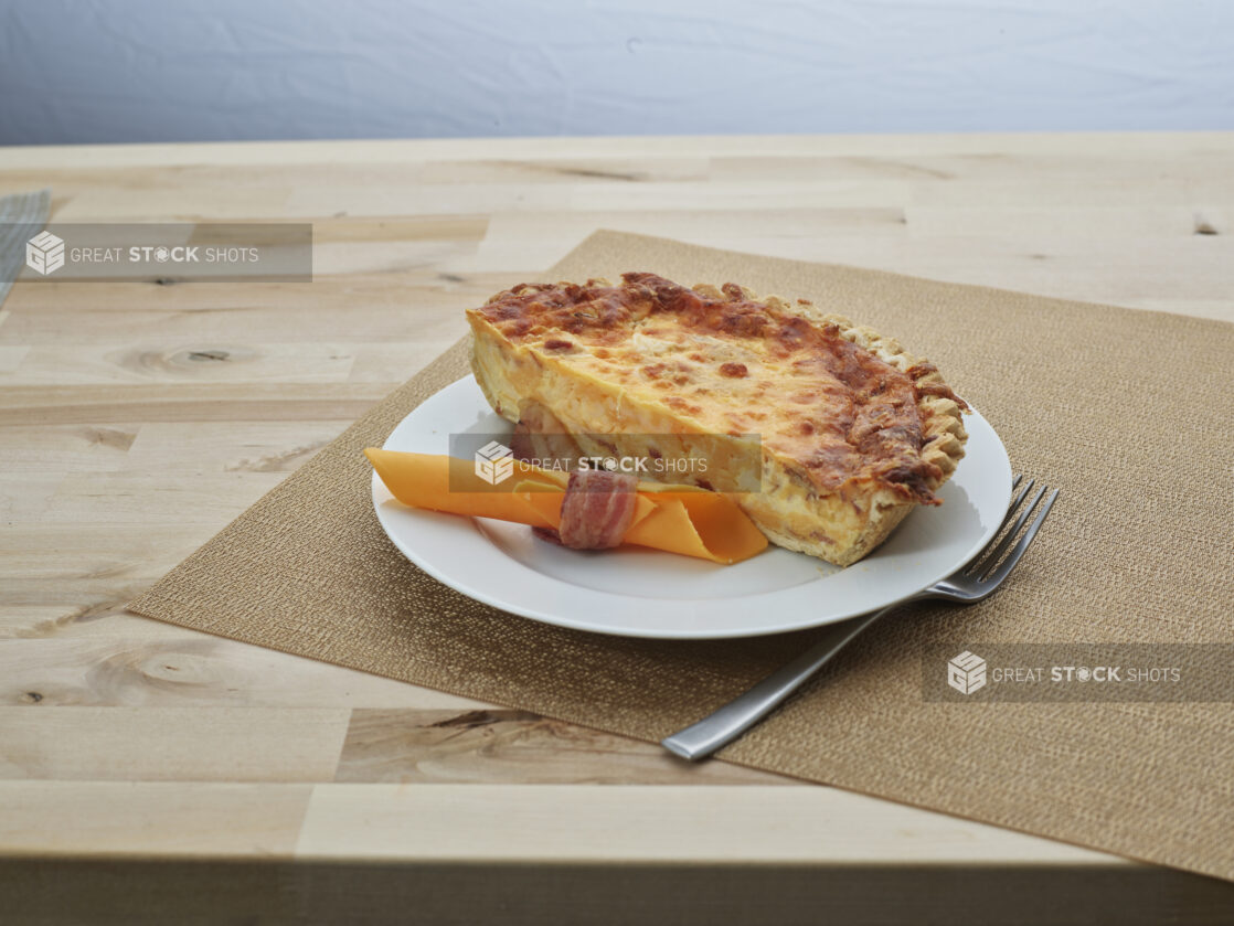 Half bacon and cheddar cheese quiche on a white plate with garnish