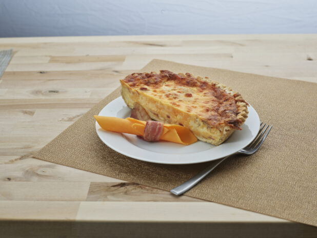 Half bacon and cheddar cheese quiche on a white plate with garnish