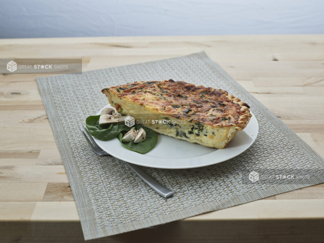 Half spinach and mushroom quiche on a white plate