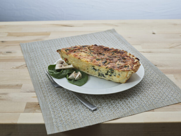 Half spinach and mushroom quiche on a white plate