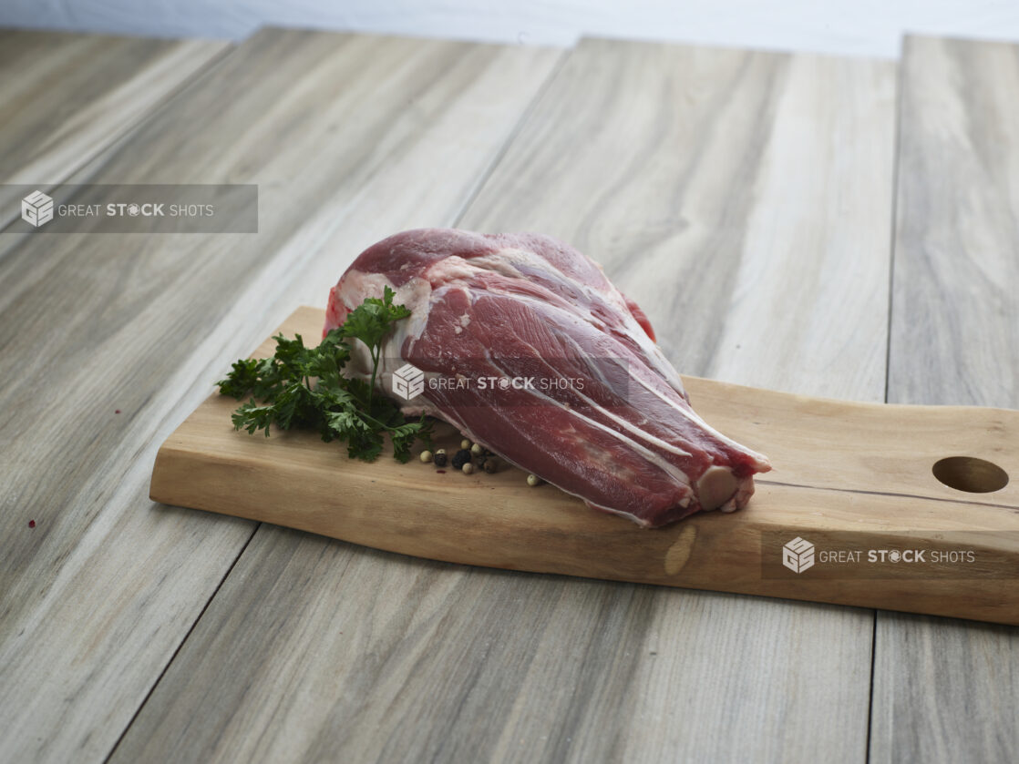 Uncooked lamb shank with seasonings on a wooden cutting board, close-up