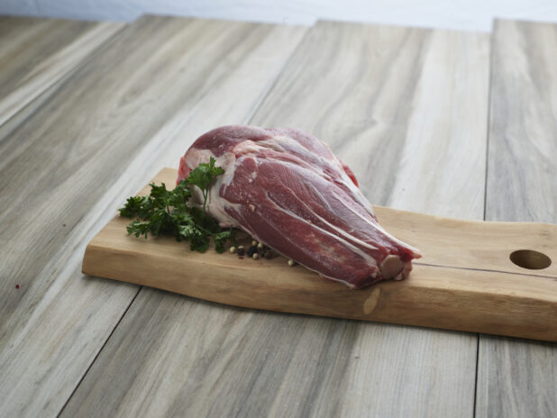 Uncooked lamb shank with seasonings on a wooden cutting board, close-up