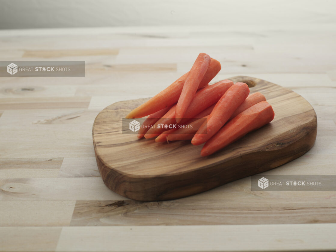 Peeled orange carrots piled on a small rounded wooden board