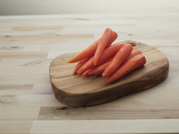 Peeled orange carrots piled on a small rounded wooden board