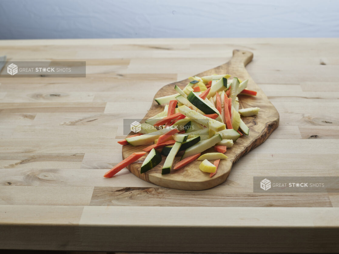 Sliced zucchini, carrots, and summer squash on a natural wood paddle, close-up