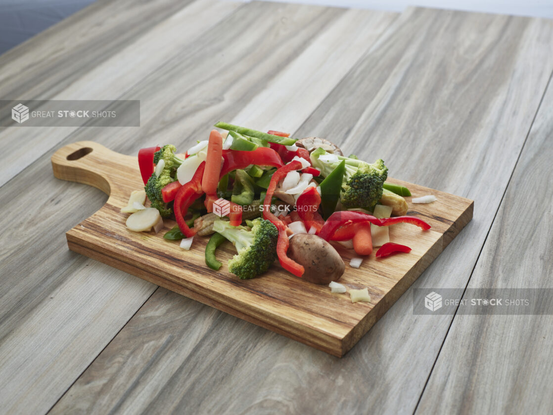 Chopped and sliced mixed vegetables on a wood paddle, close-up